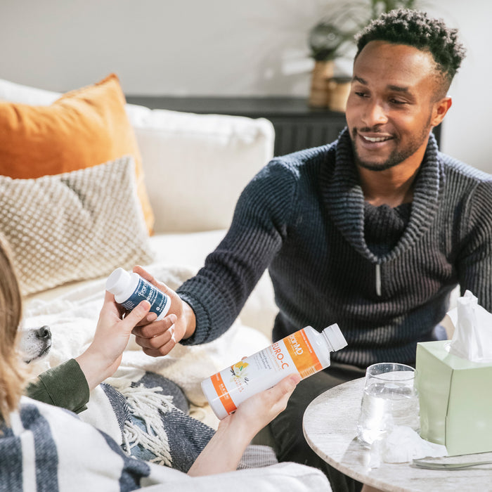 BrainMD Total Immune Health Bundle: woman holding two supplement bottles hands one to a man, living room setting