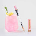 TWSBI ECO Pink Lemonade fountain pen beside a glass of pink lemonade with lemon and rosemary.