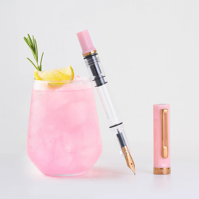 TWSBI ECO Pink Lemonade fountain pen beside a glass of pink lemonade with lemon and rosemary.