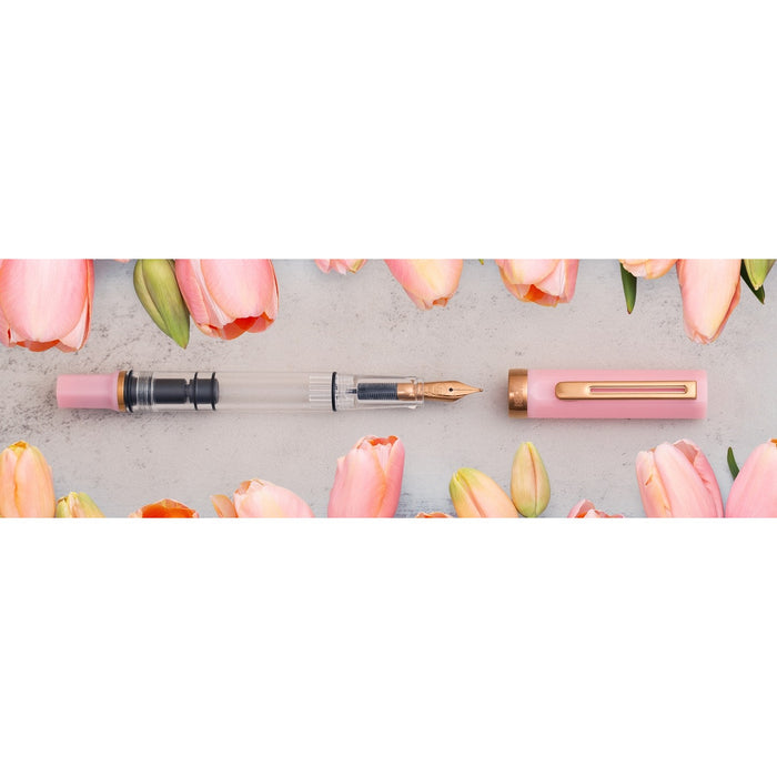TWSBI ECO Pink Lemonade fountain pen and cap laid flat on stone, framed by pale pink tulips.